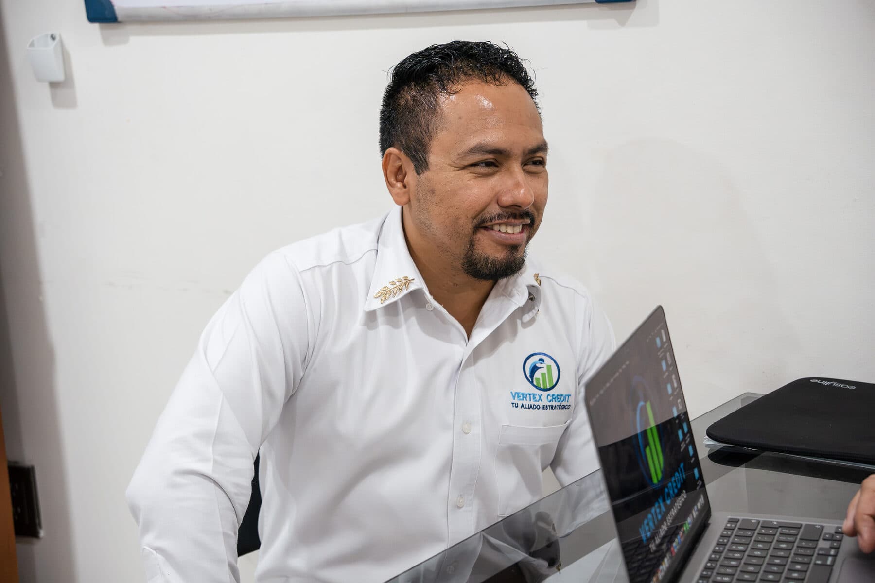 Asesor de Vertex Credit sonriendo mientras trabaja en su computadora.