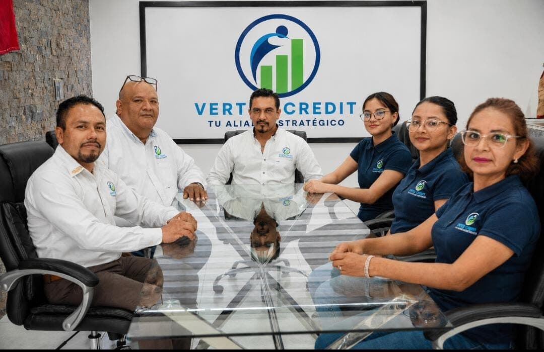 Equipo de Vertex Credit reunido en la sala de juntas, frente al logotipo de la empresa.